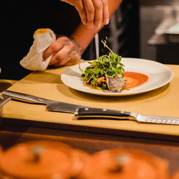 A chef finishing a plate at the kitchen pass